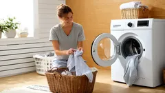 Nainen lajittelee pyykkiä pesukoneen edessä kodikkaassa pesuhuoneessa.