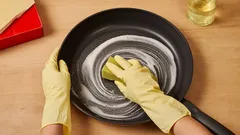 Pannun pesu keltaisin käsinein, pesusieni ja puhdistusaine, puhdas keittiö.